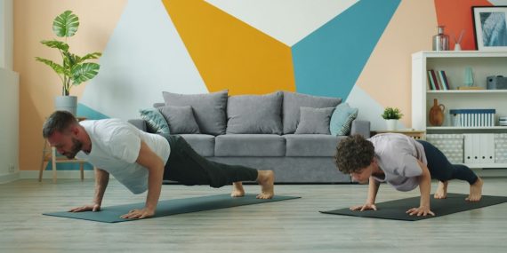 Male and female yoga students are practising downward dog position at home focused on practice on mats, people are moving simultaneously doing asanas.