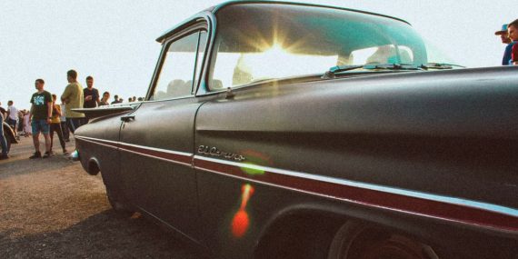 Classic Chevrolet El Camino parked under bright sunlight, surrounded by people at an outdoor event.